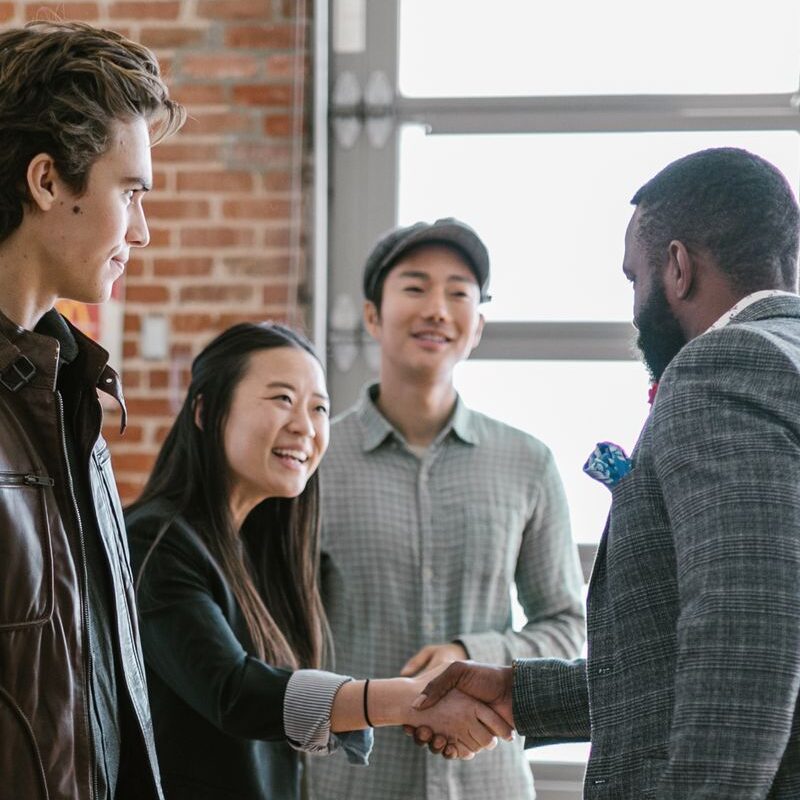 A diverse group of business professionals engaging in a handshake and discussion in a modern office space.